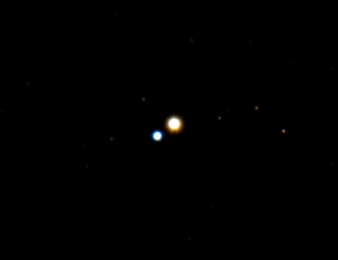 Telescope view of a bright golden yellow star beside a smaller blue star on a black starry background