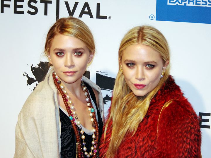 Ashley and Mary-Kate Olsen standing side by side in dark outfits at a film premiere